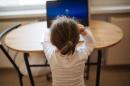 Photo of a young child working on a computer and seated at a table.